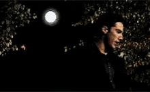 a man is standing in the dark with a full moon in the background .
