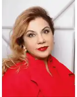 a woman wearing a red jacket and pearl earrings looks at the camera