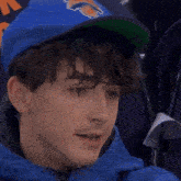 a young man wearing a green hat and a blue jacket looks up