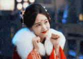 a woman wearing a red kimono and a white fur collar is smiling
