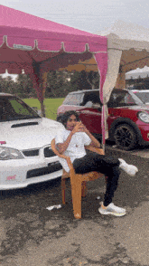 a man sits in a chair in front of a white car that says s177 on it