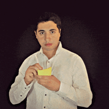 a man in a white shirt is holding a small yellow piece of paper