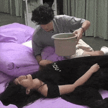 a man is holding a bucket over a woman 's stomach while she is laying on a bed .