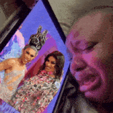 a woman is crying while looking at two drag queens on a screen