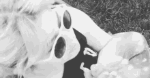 a woman is laying on the grass wearing sunglasses and a black shirt with the letter p on it .