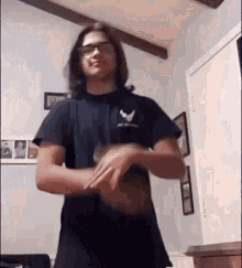 a young man wearing glasses and a black shirt is standing in a room .
