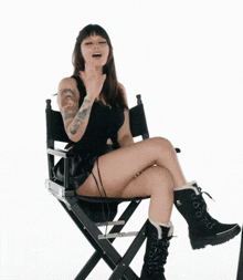 a woman is sitting on a director 's chair with her legs crossed and waving .