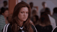 a woman in a cheerleading uniform is standing in front of a crowd of people and looking at the camera .