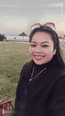 a woman wearing sunglasses and a necklace smiles for a selfie