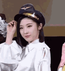 a woman wearing a pilot hat and a white shirt is looking at the camera .