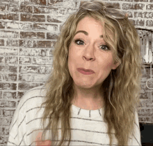 a woman wearing glasses and a striped shirt making a funny face in front of a brick wall