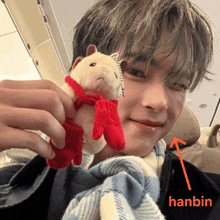 a man is holding a stuffed animal with a red scarf around its neck and the name hanbin is next to the stuffed animal