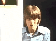 a young man in a blue shirt is standing in a doorway .