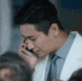 a close up of a man in a white coat and tie talking on a cell phone .