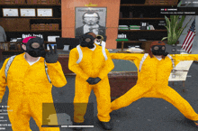 three people wearing yellow jumpsuits and gas masks pose in front of a portrait of a man named damon