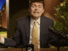 a man in a suit and tie is standing in front of a microphone with his arms outstretched
