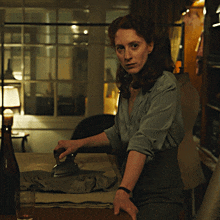 a woman is ironing a piece of cloth in a room with a window behind her