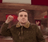 a man in a brown jacket is waving his hand in front of a red background .