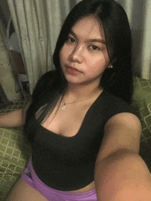 a woman wearing a black top and purple shorts is taking a selfie