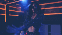 a woman in a black dress is dancing in a dark room in front of a blue light .