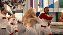 a group of people are dancing in front of a building that says disney plus