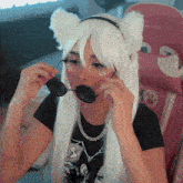 a woman wearing a cat ears headband and sunglasses is sitting in a pink chair