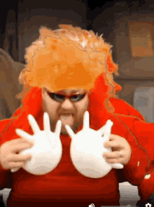 a man wearing a red wig and sunglasses is holding up his hands