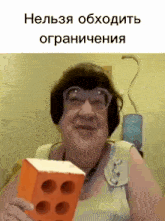 a woman wearing glasses is holding an orange brick in her hand