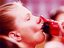 a close up of a woman drinking from a red bottle with the word coca cola on it