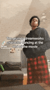 a man is standing in a living room wearing plaid pajamas and a black hoodie .