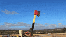 a large red and yellow axe is being thrown in a field with a blue sky in the background