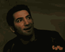 a man is smiling in a dark room and the name gamar is on the bottom right