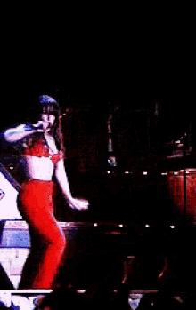 a woman in red pants singing into a microphone on a stage