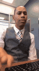 a man in a suit and tie is sitting at a desk with a keyboard .