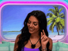 a woman in a purple top is smiling in front of a palm tree and ocean