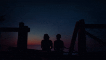 a man and a woman sit on a fence looking at the stars