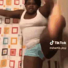 a woman in a white tank top and blue shorts is doing a split in front of a colorful shower curtain .