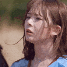 a close up of a woman 's face with a blue shirt and a necklace .