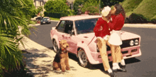a couple kissing next to a pink car