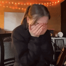 a woman covering her face with her hands in a room with a guitar