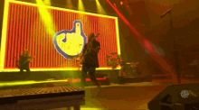 a man playing a guitar on stage in front of a large screen with a middle finger on it