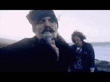 a man is singing into a microphone while another man stands behind him