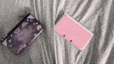 a pink nintendo 3ds is laying on a bed next to a purple case