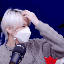 a man wearing a mask adjusts his hair while standing in front of a now microphone