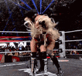 two women are wrestling in a wrestling ring while a crowd watches .