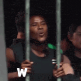 a man is standing behind bars in a prison cell talking on a cell phone .