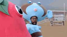 a man in a blue and brown costume stands next to a red tomato