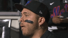 a man wearing a mets hat has a black patch on his face .