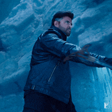 a man in a black leather jacket is standing in front of a blue wall