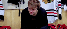 a young man is sitting in a locker room with a hockey jersey hanging on the wall behind him .